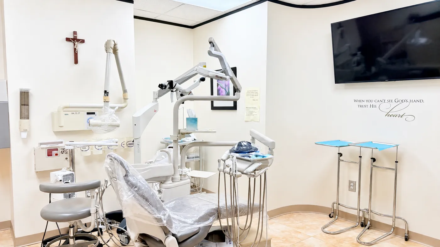 A SoftDental exam room showing the Leica microscope, dental chair, and scripture wall art reading 'When you can't see God's hand, trust His heart'